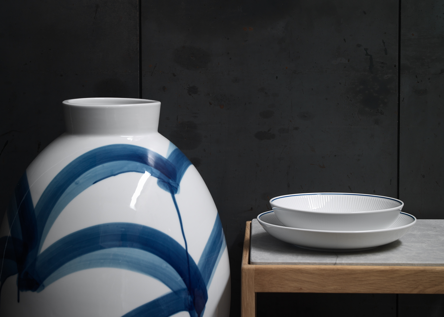 A Blueline deep plate and Blueline Bowl stacked on a table next to a very large vase